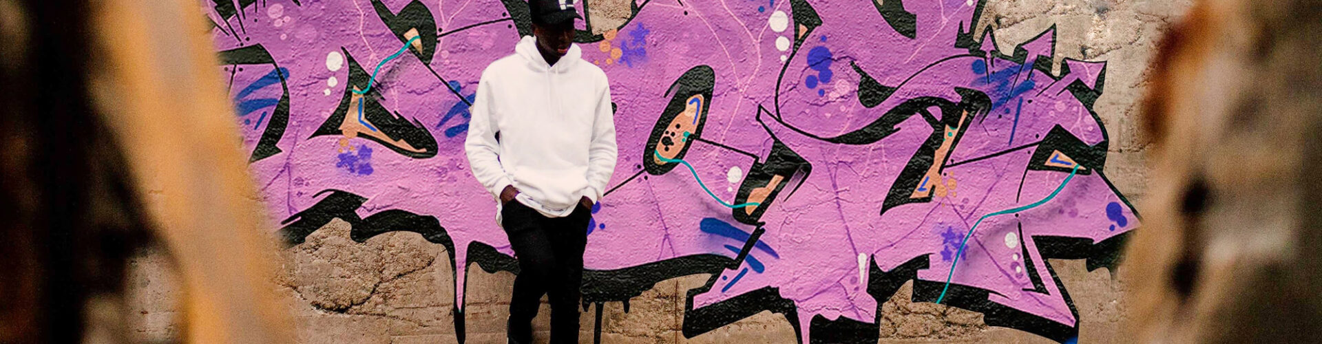 Young Black man stands in front of a wall of graffiti